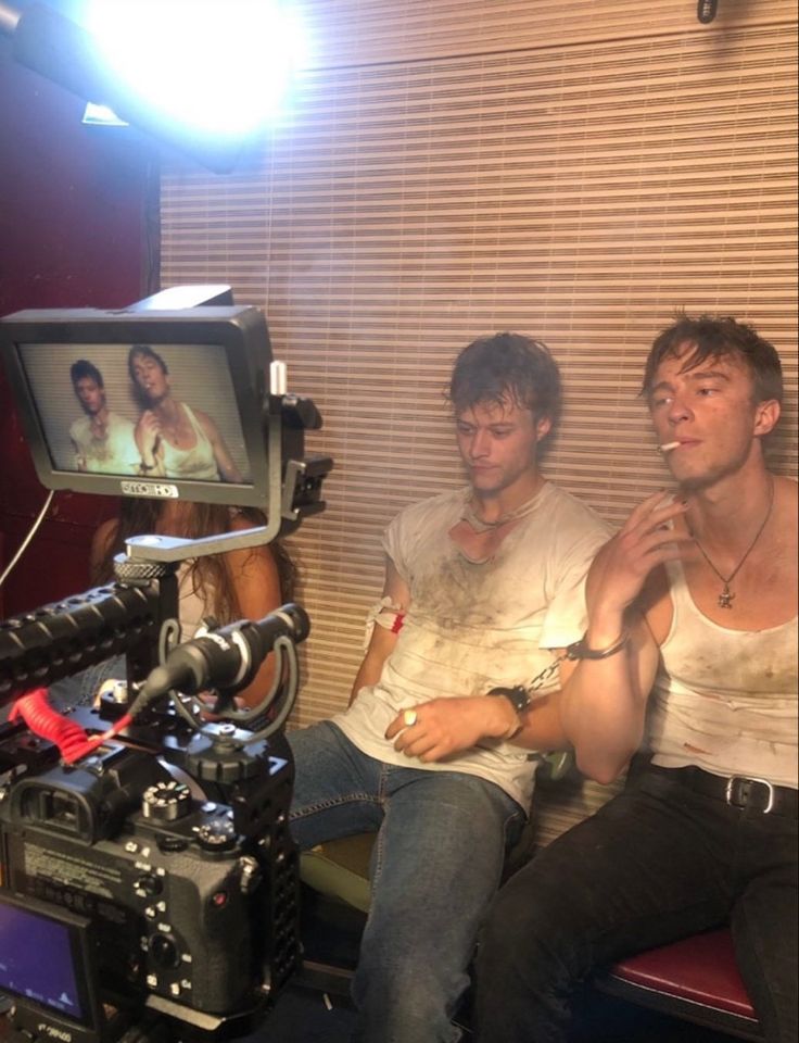 two men sitting next to each other in front of a camera and television set with lights on