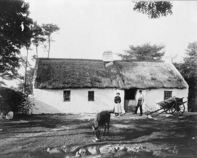 an old black and white photo of two men standing in front of a thatched house