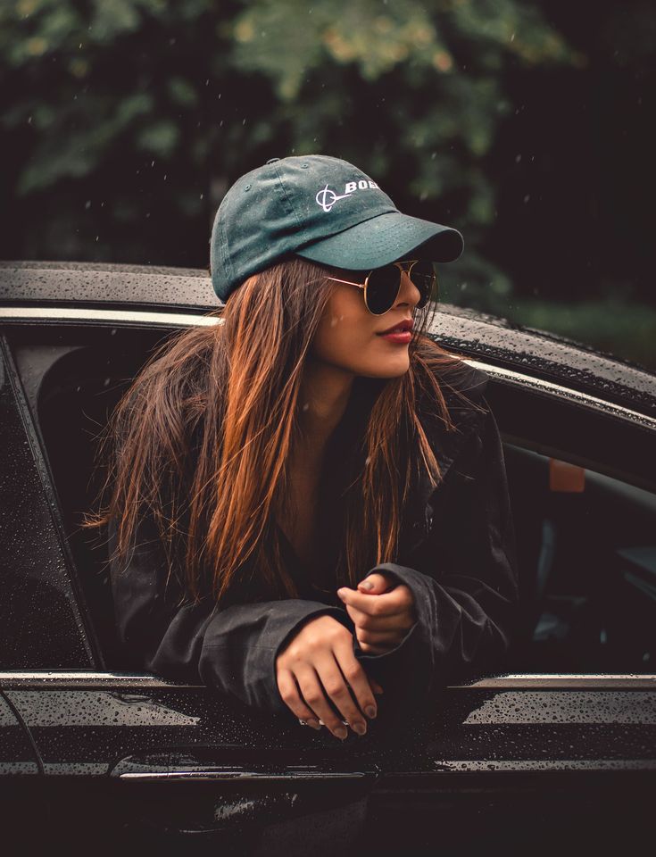 a woman in sunglasses and a hat leaning out the window of a car