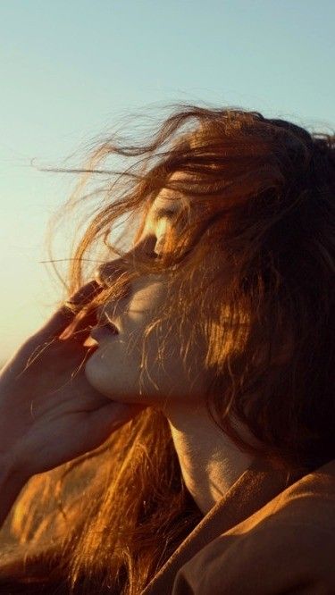 a woman with long hair is talking on her cell phone while standing in the sun