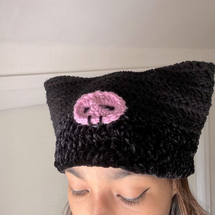 a woman wearing a black knitted hat with a pink button on the front and side