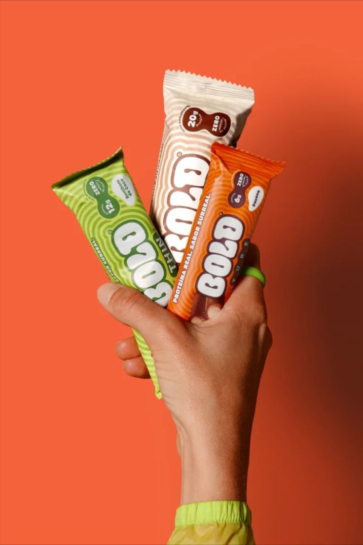 a hand holding three candy bars on an orange background