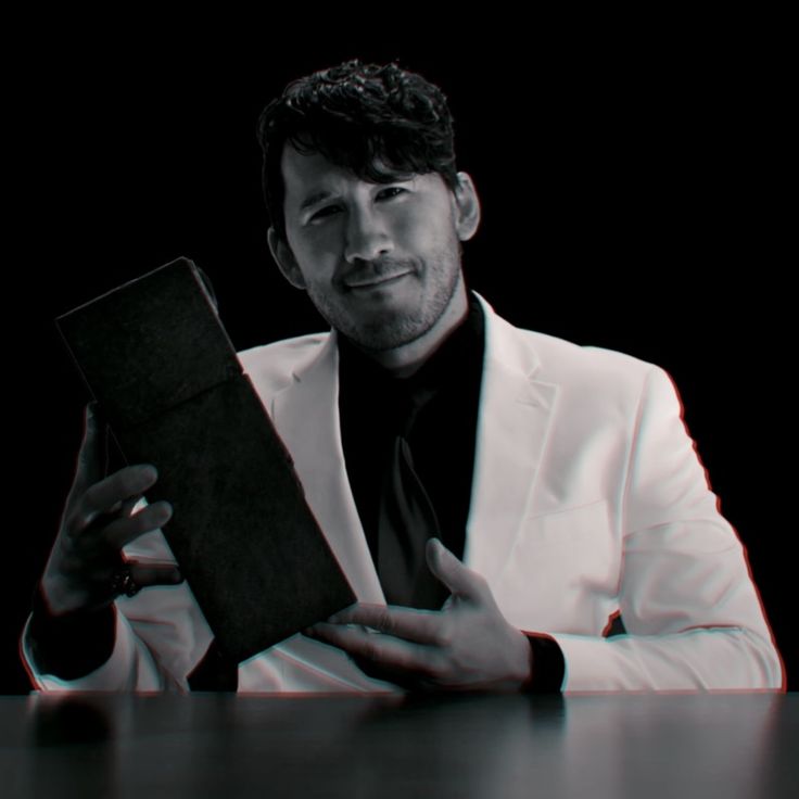 a man in a white suit is holding a black book while sitting at a table