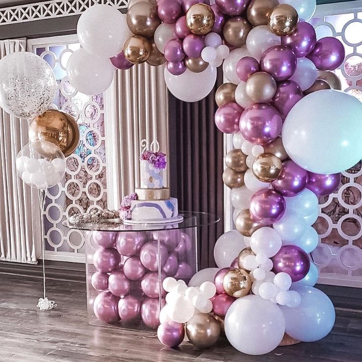 a table topped with lots of balloons next to a tall white and gold letter shaped cake