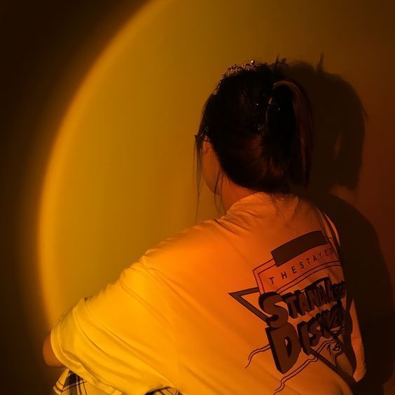 a woman in a yellow shirt is sitting on a stool with her back turned to the camera