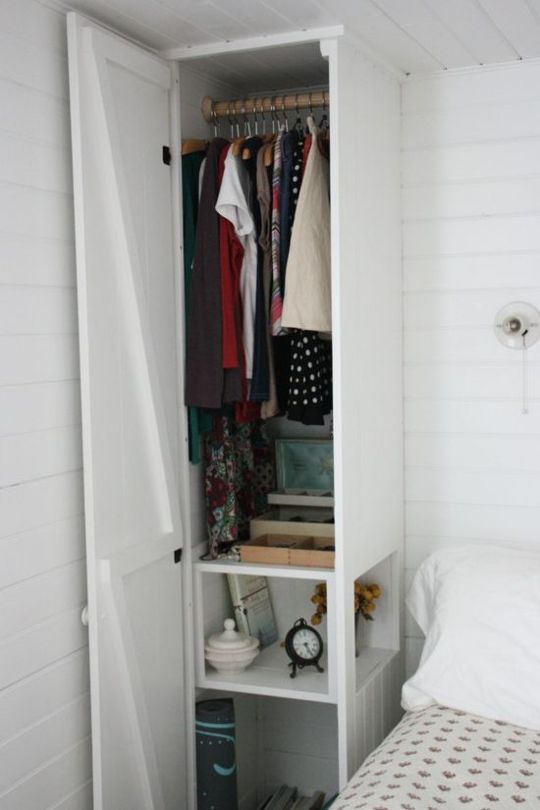 a white closet with clothes hanging on the rails and an unmade bed in front of it