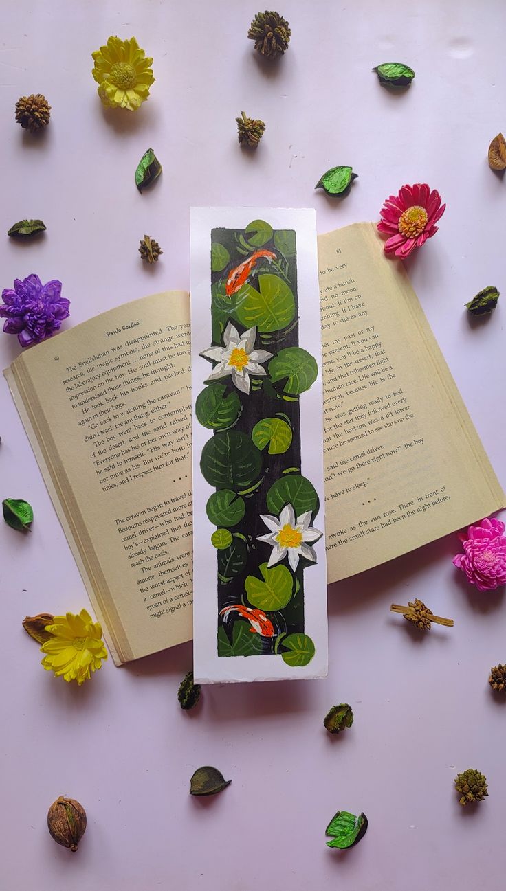 an open book laying on top of a table with flowers and leaves around the pages