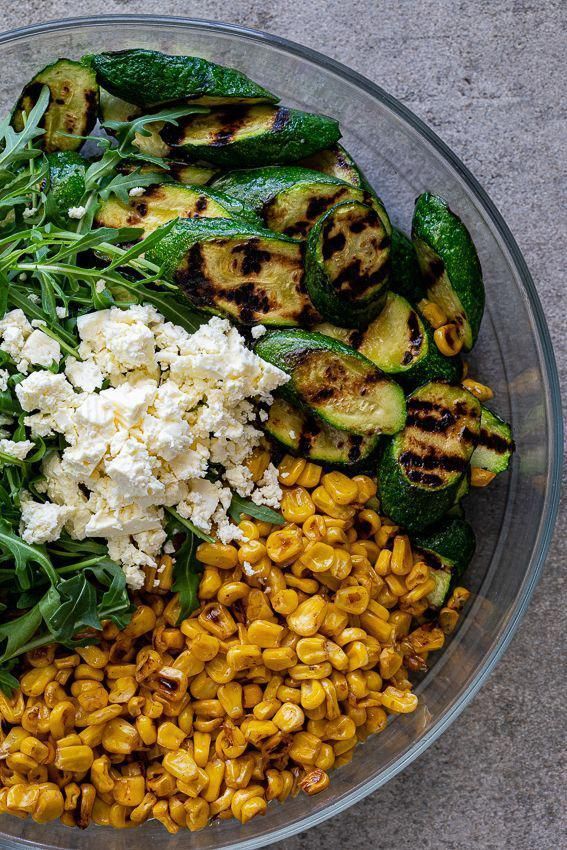 a glass bowl filled with corn, zucchini, and other vegetables on top of a table