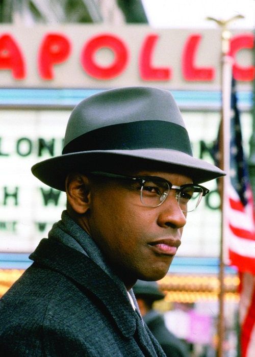 a man wearing glasses and a hat standing in front of a sign with an american flag