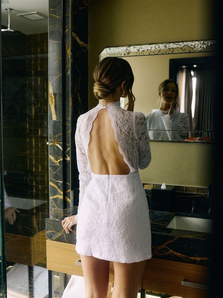 a woman standing in front of a mirror wearing a white dress