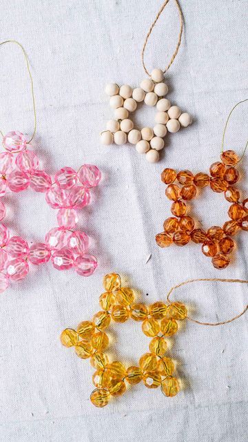 four beaded ornaments are shown on a white tablecloth with twine and beads