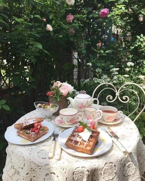 the table is set with tea and waffles for two people to enjoy in the garden