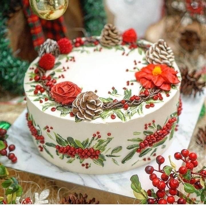 a decorated cake sitting on top of a table next to pine cones and red berries