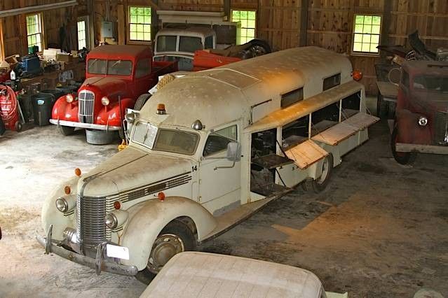 an old school bus is parked in a garage with other cars and trucks behind it