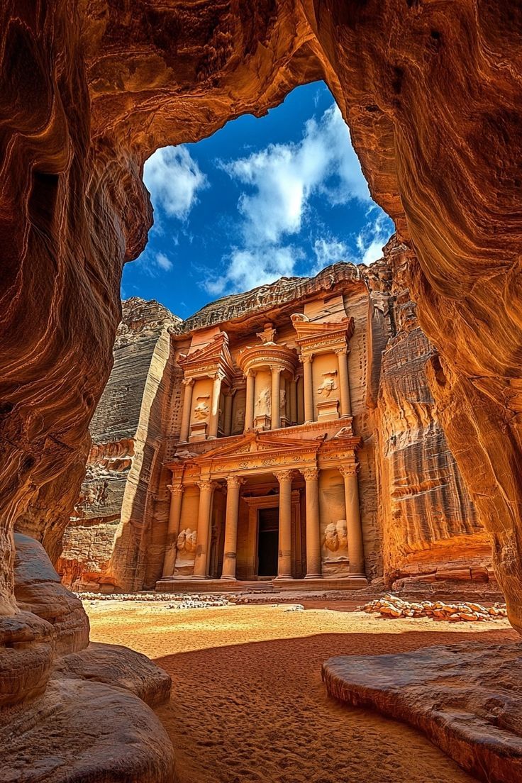 an ancient building in the middle of a desert with large rocks surrounding it and a sky filled with clouds