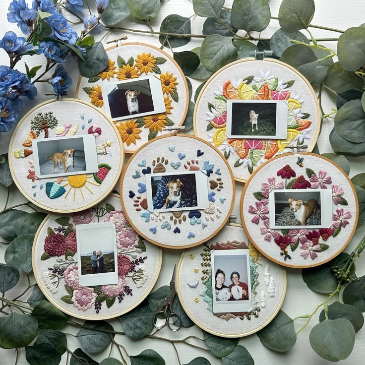 four embroidered plates with pictures on them and flowers in the middle one is surrounded by greenery