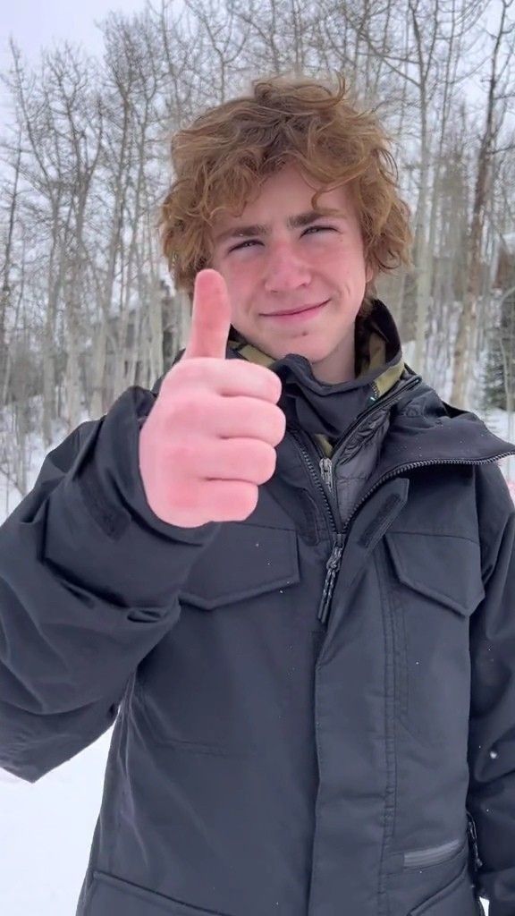 a young man is giving the thumbs up sign in front of some snow covered trees