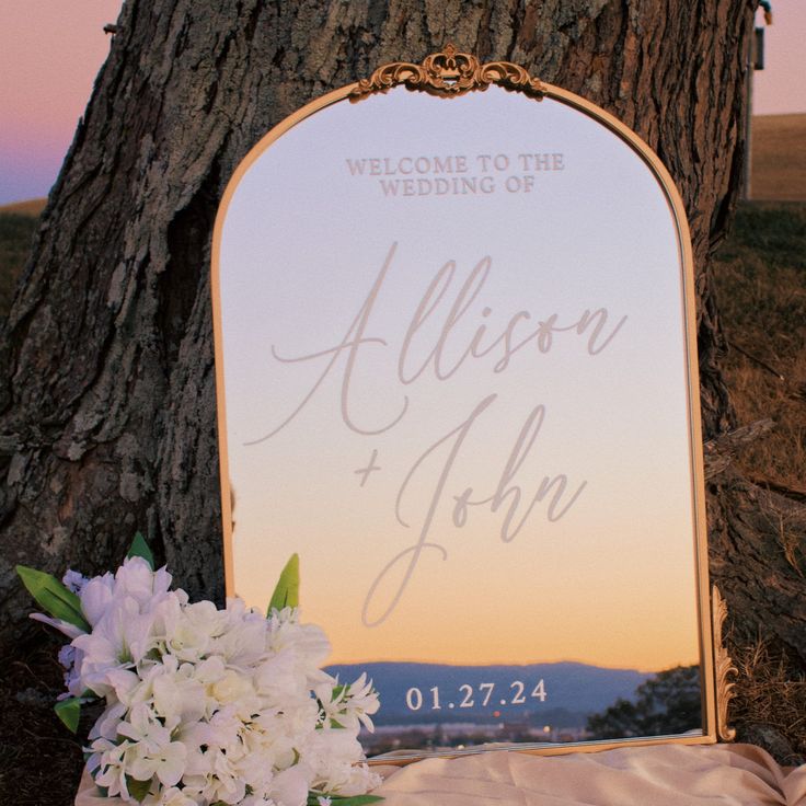 a wedding sign sitting on top of a tree next to a vase filled with flowers