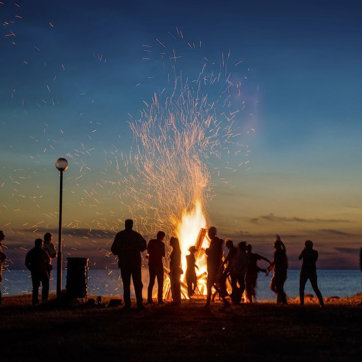 a group of people standing around a fire pit at night with fireworks in the sky