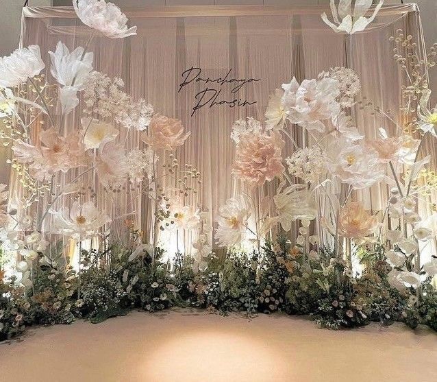 an arrangement of flowers and greenery is displayed on the wall in front of a backdrop