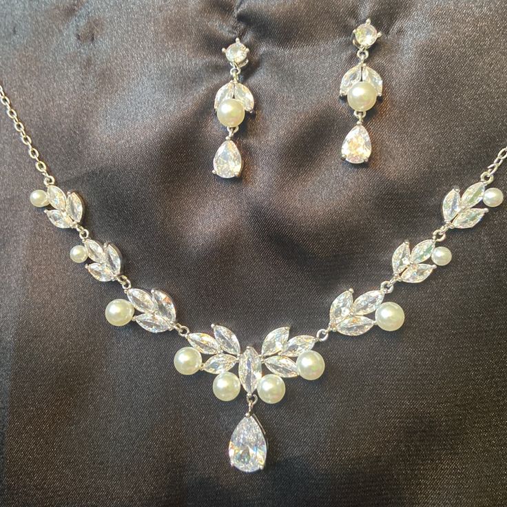 a necklace and earring set is shown on a black cloth with pearls, crystals and leaves