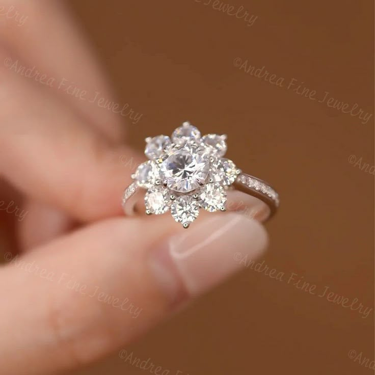 a woman's hand holding an engagement ring with three stone flowers on the side