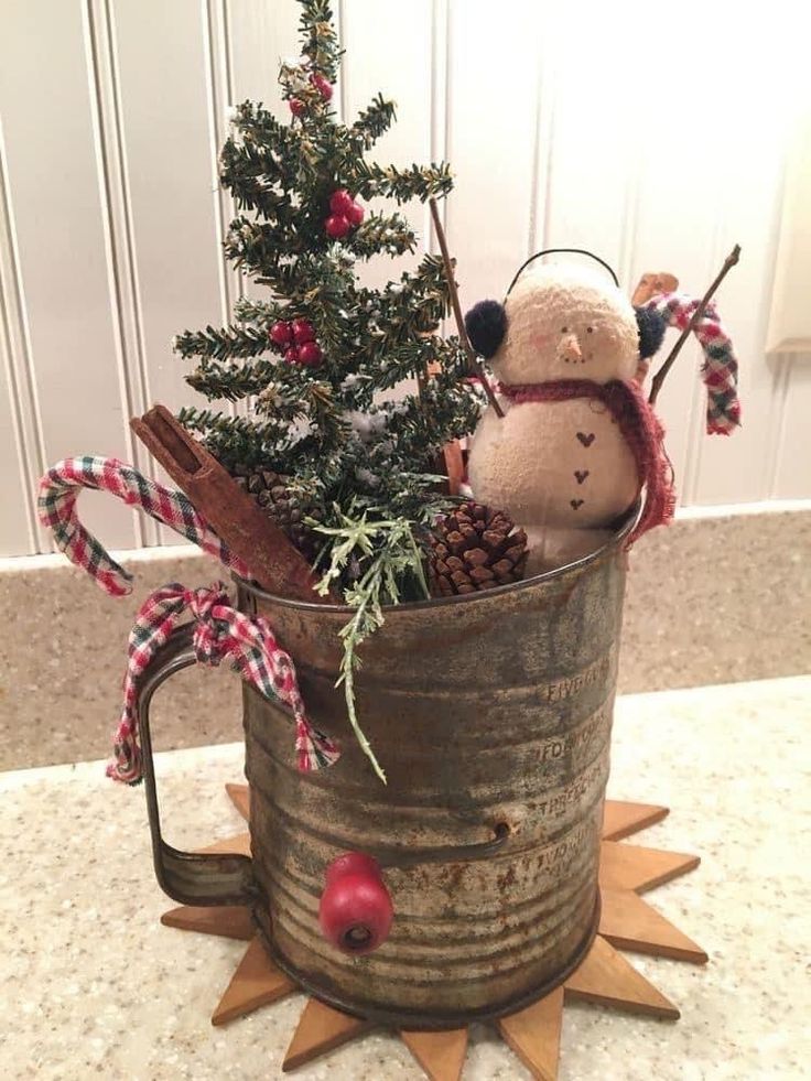 a small christmas tree in an old metal mug with a teddy bear and snowman