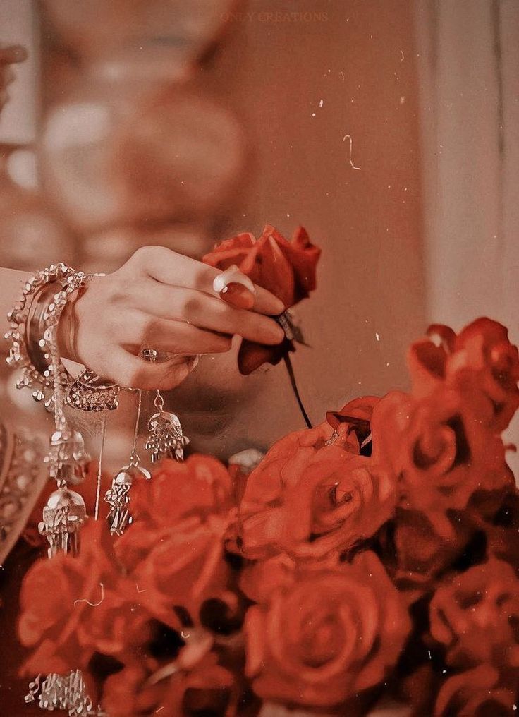 a woman is holding a rose in her hand and looking down at the roses that are being held by her hands