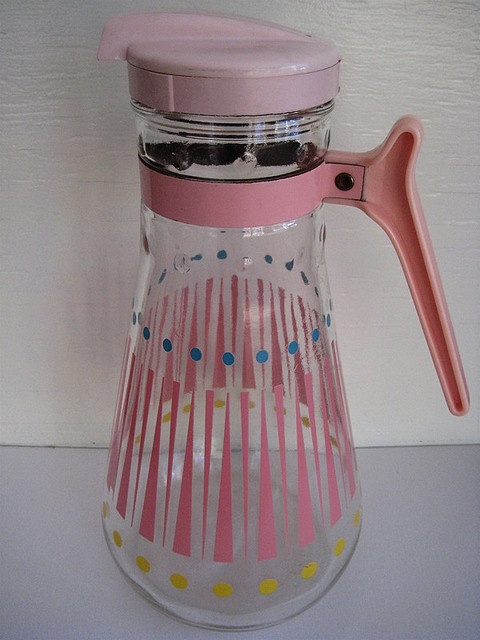 a pink and white glass pitcher sitting on top of a counter next to a wall