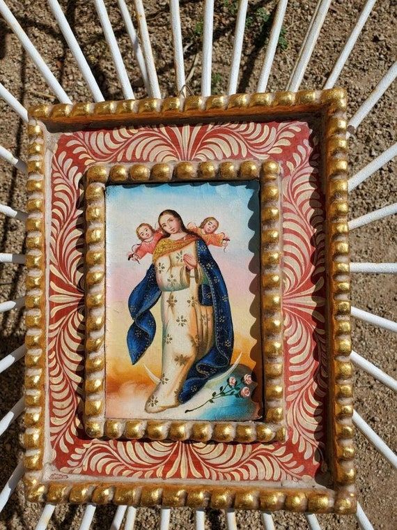 an image of the virgin mary in gold and blue on a wooden frame with white sticks sticking out of it