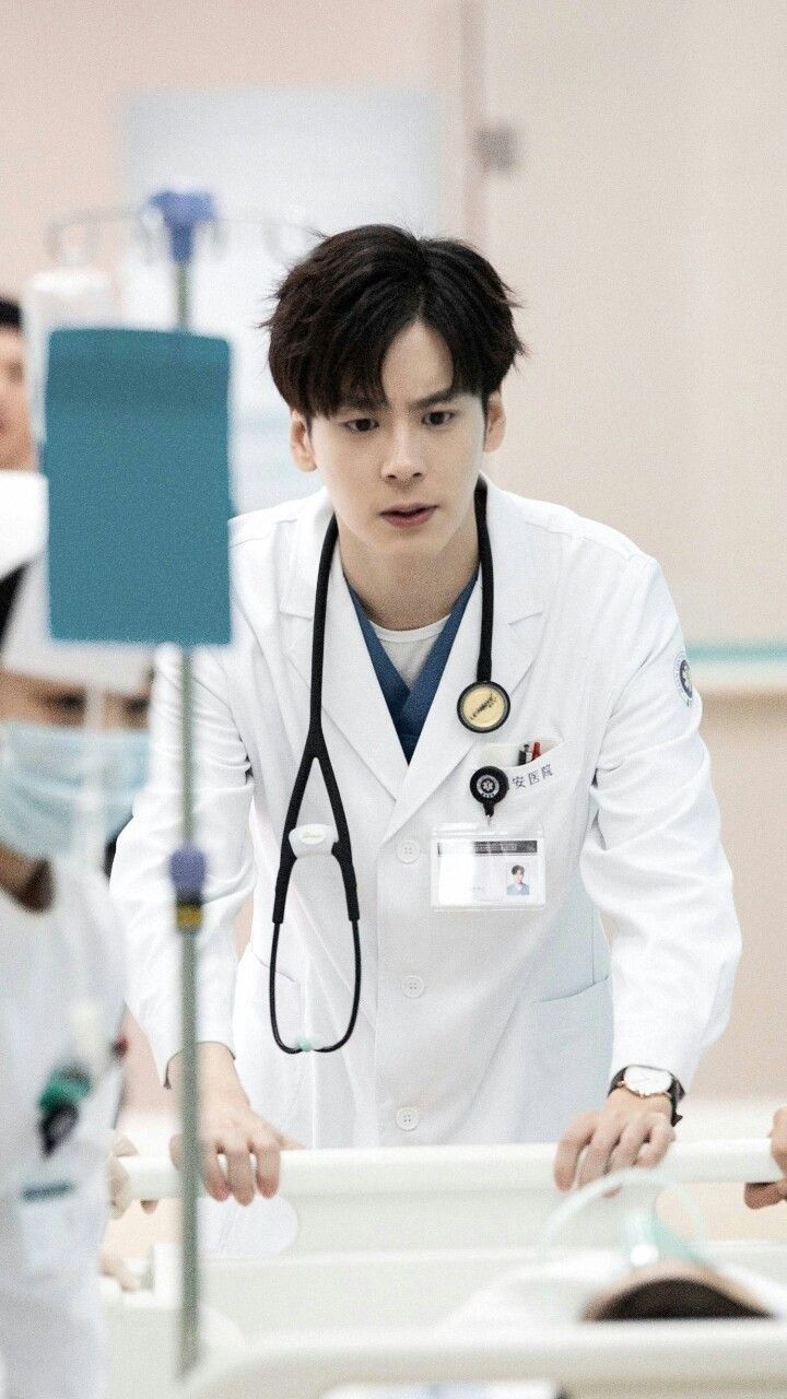 a male doctor wearing a white coat and stethoscope standing next to a bed