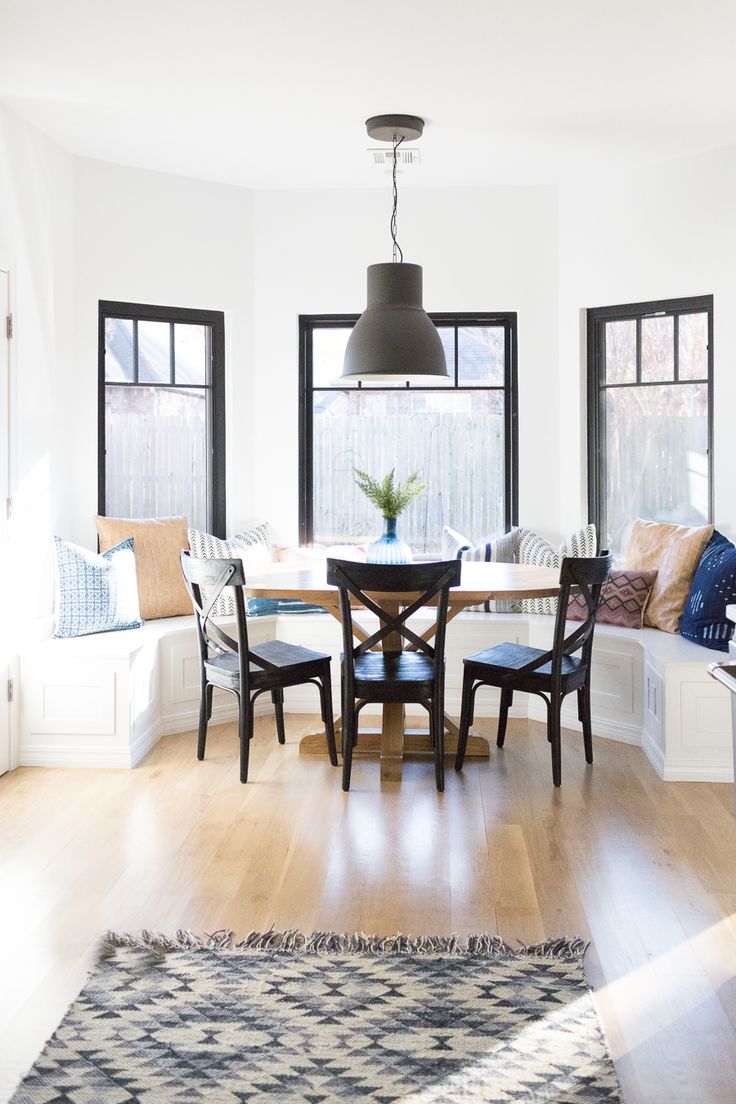 a dining room table with four chairs and a bench in front of the window is surrounded by windows