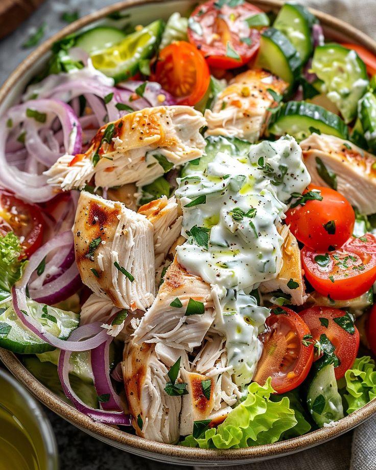 a salad with chicken, tomatoes, cucumbers, onions and dressing in a bowl