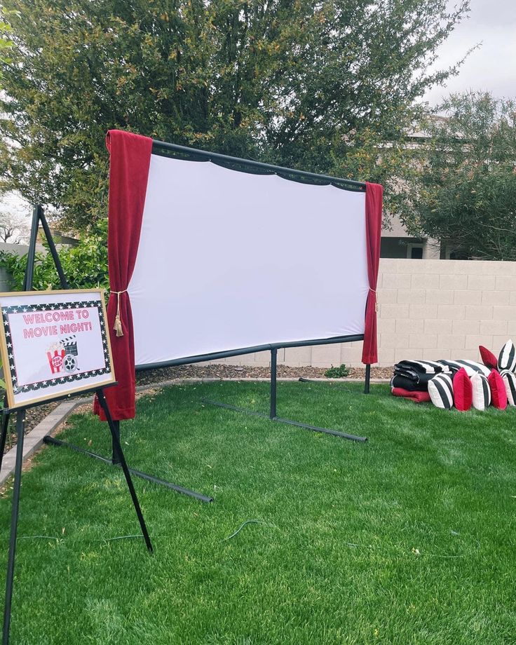 an outdoor movie set up in the grass with a white screen and red drapes