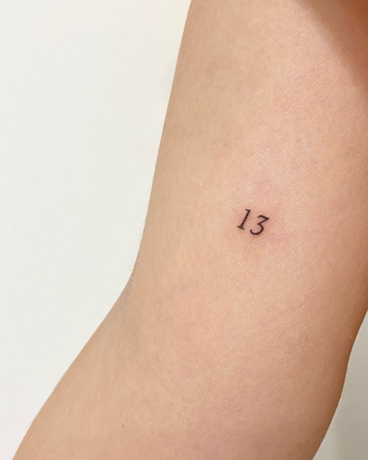 a woman's arm with a small tattoo on it that says 13 in black ink