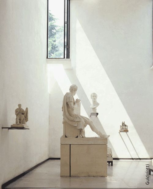 a room filled with statues and windows next to each other in white walls, on either side of the wall is a window