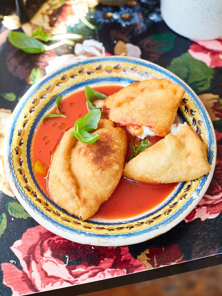 two dumplings are in a bowl with tomato sauce and sour cream on the side