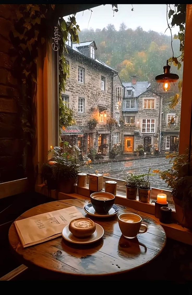 a table with two cups and saucers on it in front of a window