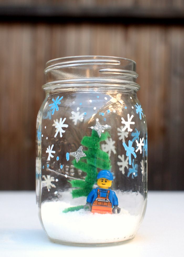 a glass jar filled with snow and a small lego man in front of a christmas tree