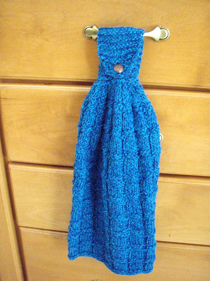 a blue knitted towel hanging from a hook on a wooden cabinet door with drawers in the background