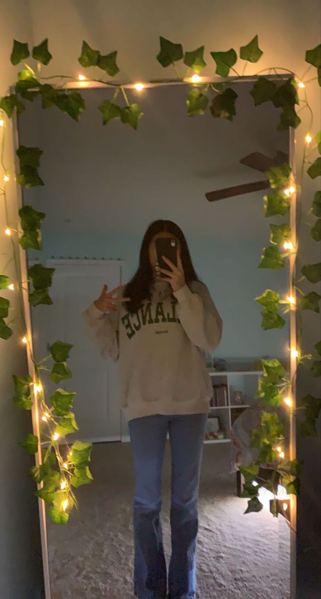 a woman taking a selfie in front of a mirror with ivy garland on it