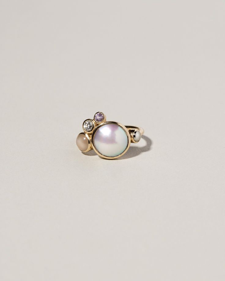 an image of a ring with pearls and stones on the front, sitting on a white surface