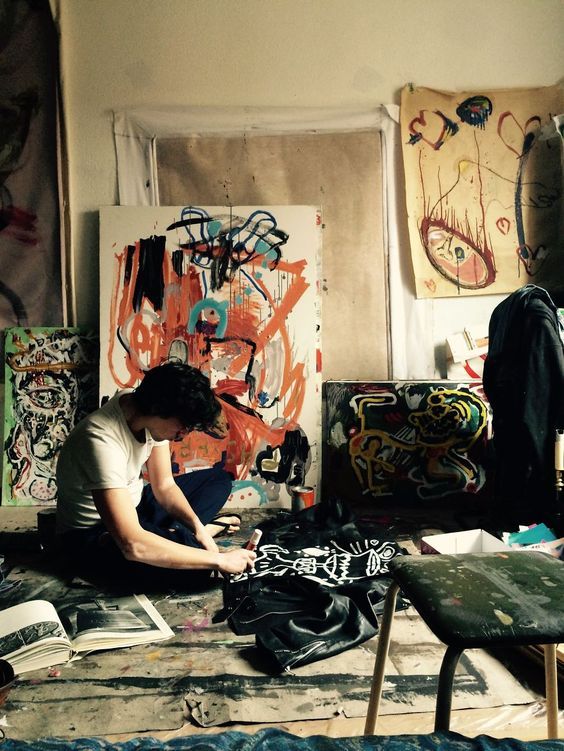 a person sitting on the floor in front of some paintings and papers with an open book