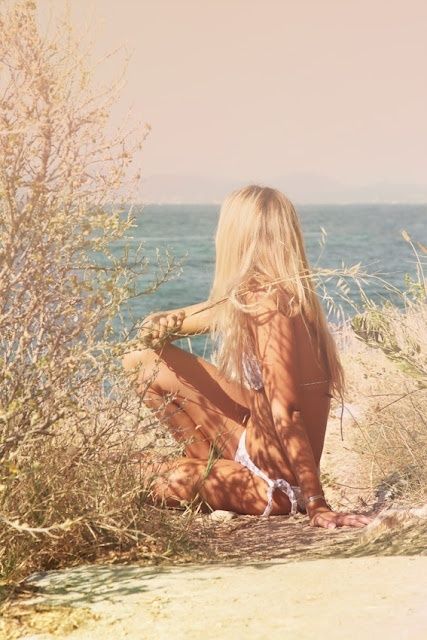 a woman sitting on top of a sandy beach next to the ocean