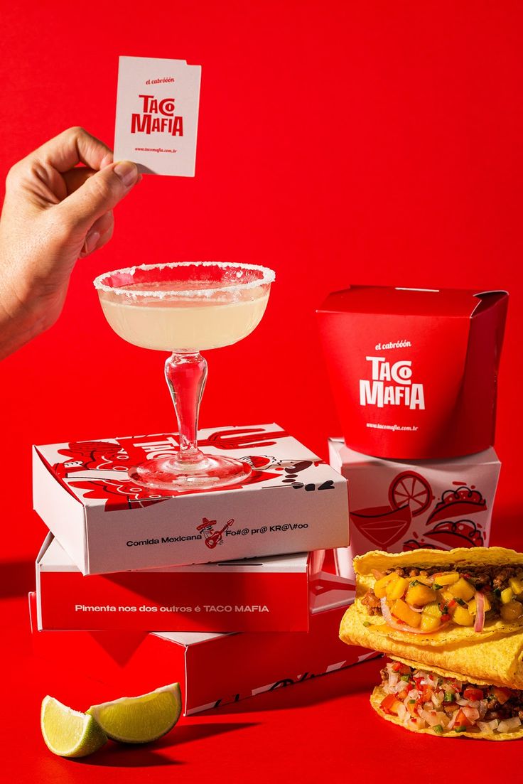 a person holding up a card next to some taco and margaritas on red background