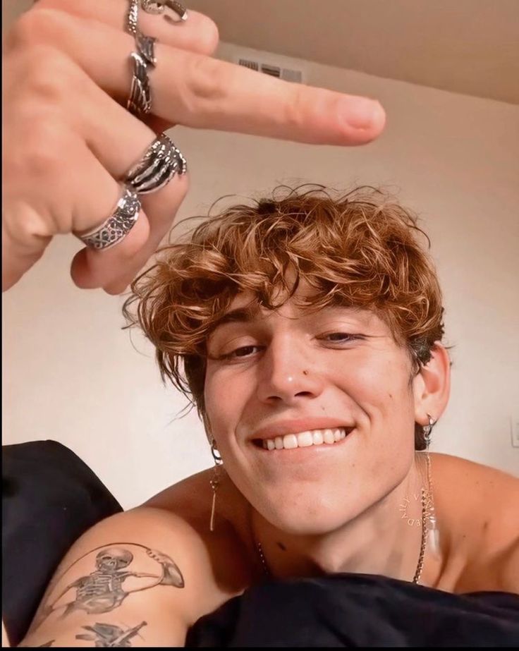 a young man with tattoos on his arm and fingers pointing at the camera while smiling