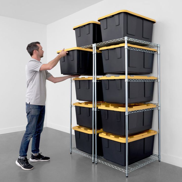 a man standing in front of a shelf filled with black boxes and yellow bins