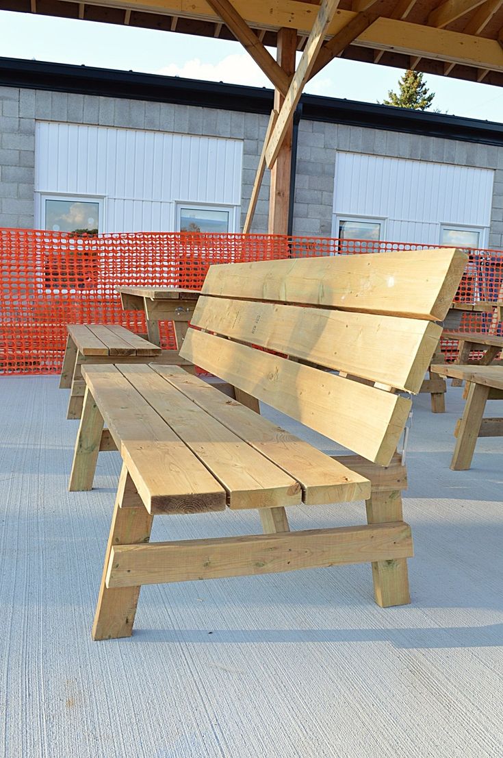 several wooden benches sitting under a roof near some orange barricade barriers and buildings