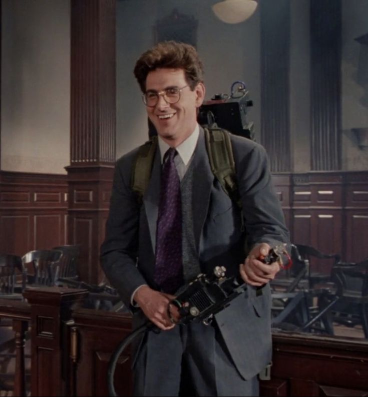 a man in a suit and tie is holding a camera while standing next to a desk