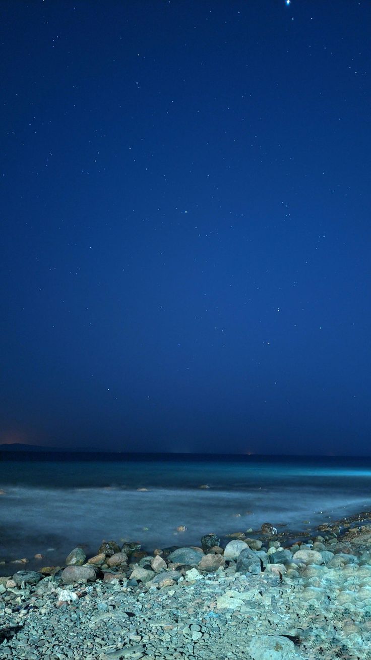 the night sky is full of stars above the ocean and rocks on the shore line